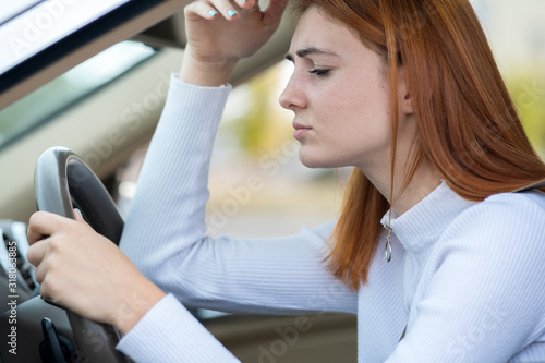 Sad tired yound woman driver sitting behind the car steering wheel in traffic jam.