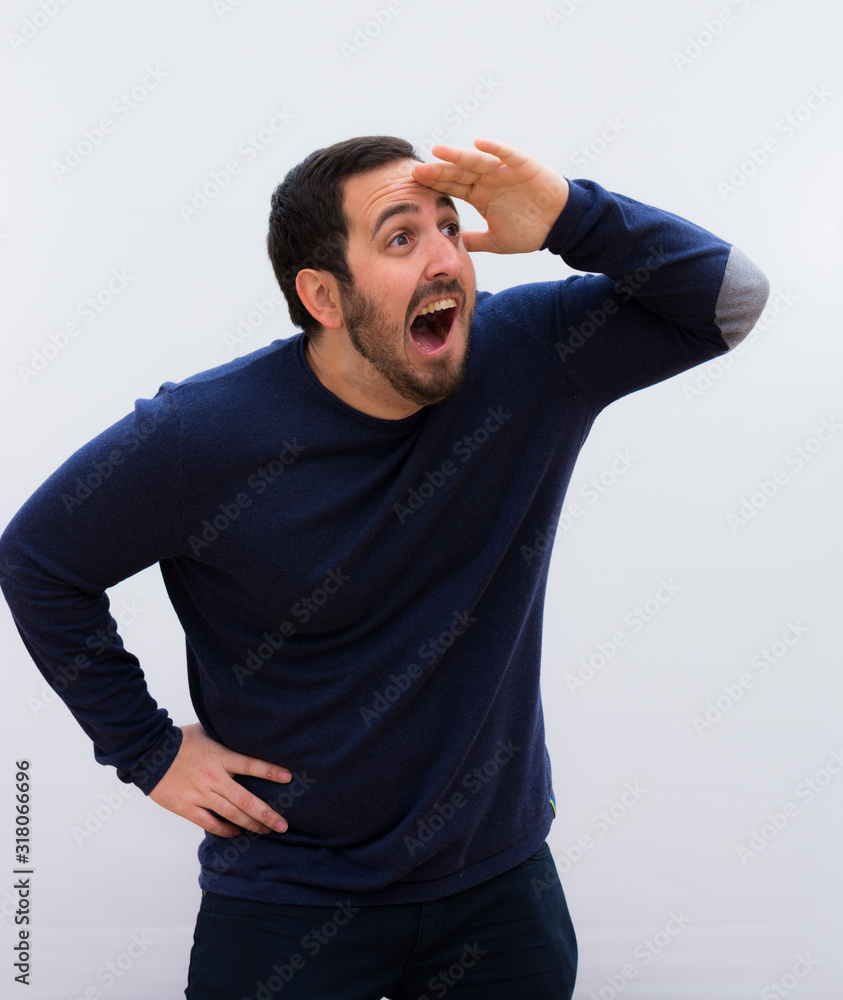 young handsome man looking bewildered and astonished, with hand over forehead looking far away, watching or searching against white wall. young handsome man looking bewildered and astonished, with hand over forehead looking far away, watching or searching against white wall.