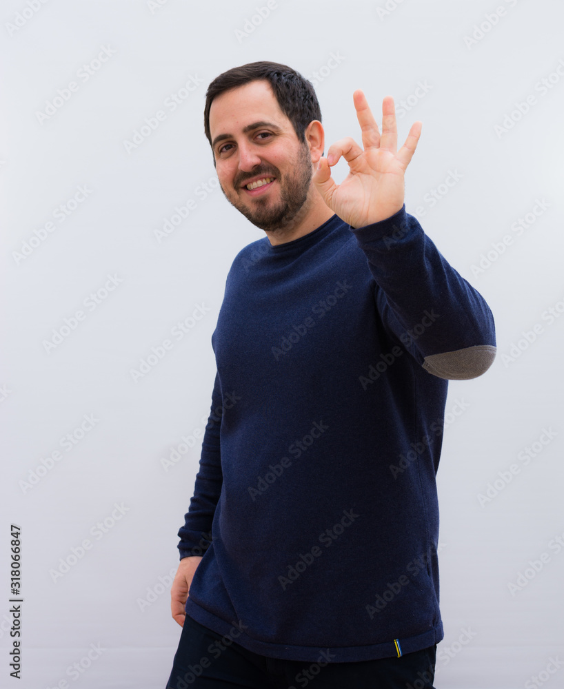 young handsome man feeling happy, relaxed and satisfied, showing approval with okay gesture, smiling against white wall young handsome man feeling happy, relaxed and satisfied, showing approval with okay gesture, smiling against white wall