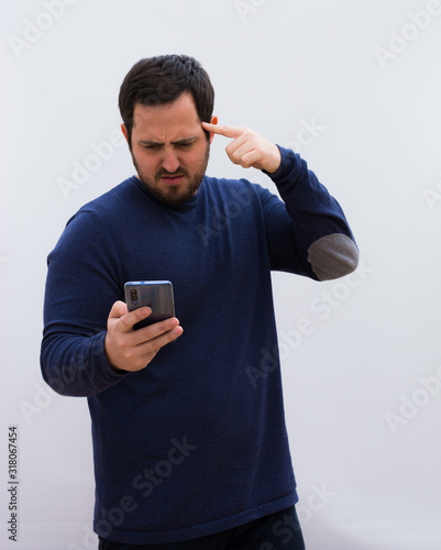 young handsome man, feeling angry with his phone, making the crazy sign to the mobile against a white wall.