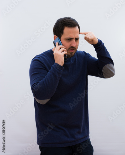 young handsome man, feeling angry with his phone, making the crazy sign to the mobile against a white wall.