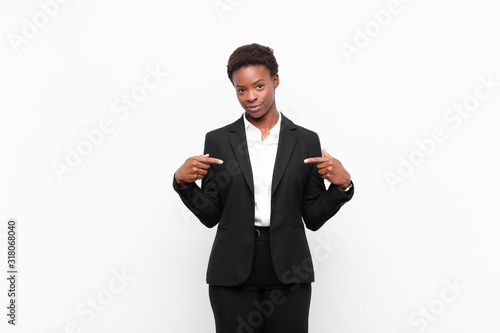 young pretty black womanlooking proud, positive and casual pointing to chest with both hands against white wall photo