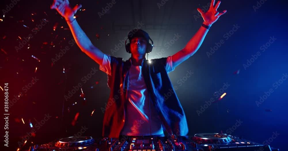 Cool dj standing at a mixer controller composing a dance music list, dancing while spotted by nightclub colorful lights - nightlife concept 4k footage