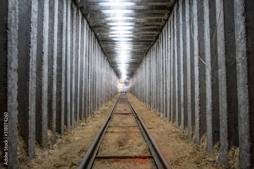 Fototapeta Naklejka Na Ścianę i Meble -  Underground square tunnel with rails for minecart and lighttrail.