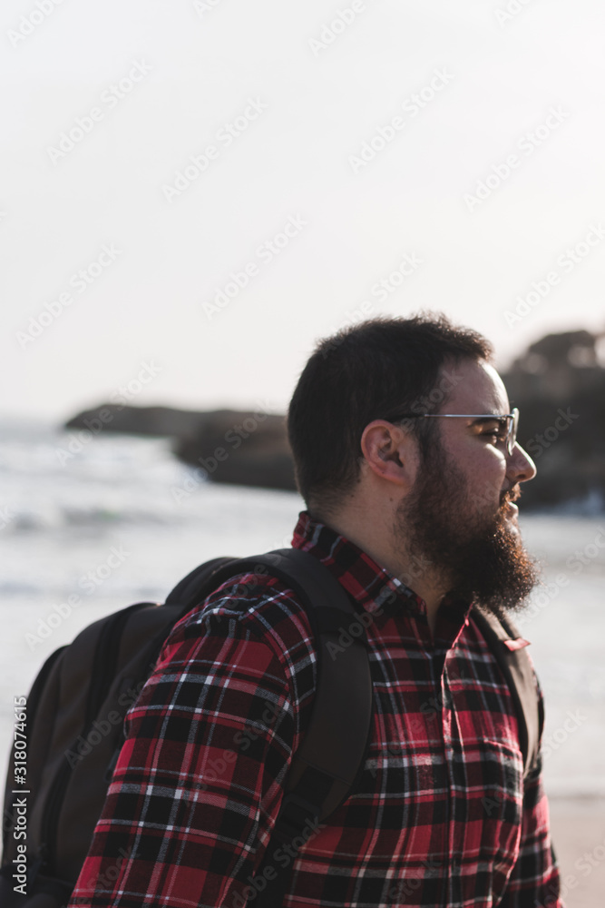 young man on the beach with backpack, glases and beard at sunset young man on the beach with backpack, glases and beard at sunset