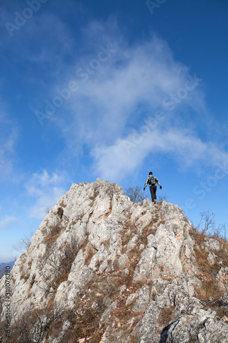 Mountain hiker with hood, backpack and gloves walking over narrow, dangerous, rocky mountain ridge