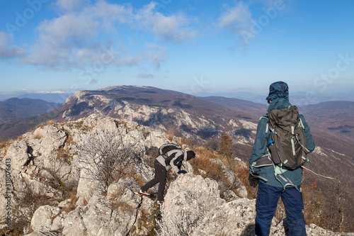 Two mountain hikers trying to pass over narrow, dangerous, slippery, rocky mountain ridge on a windy day with phantom blue sky © Nikola