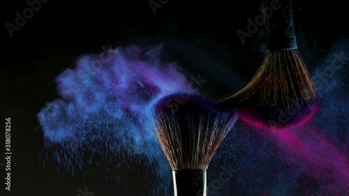 Two Soft cosmetic brushes release a cloud of colored smoke from bright eyeshadow and powder, photo