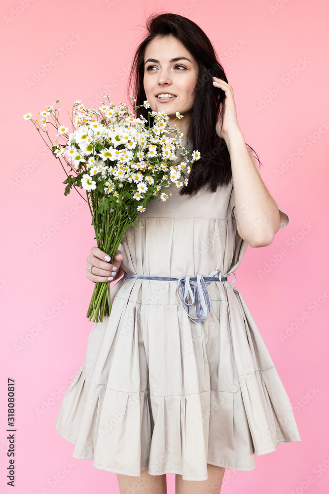 Girl in a dress with a bouqet of flowers chamomile on a pink background in front of camera Girl in a dress with a bouqet of flowers chamomile on a pink background in front of camera