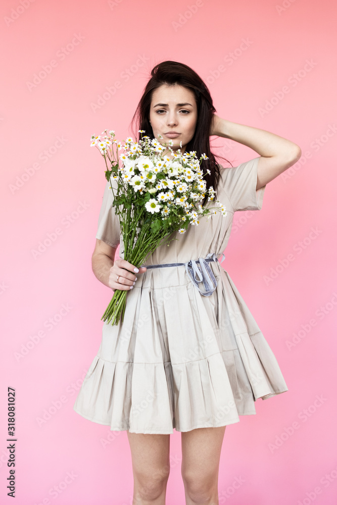 Girl in a dress with a bouqet of flowers chamomile on a pink background in front of camera Girl in a dress with a bouqet of flowers chamomile on a pink background in front of camera