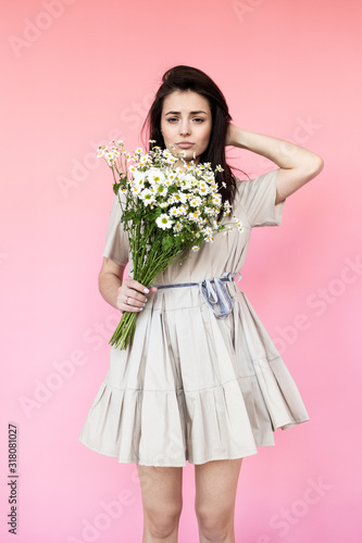 Girl in a dress with a bouqet of flowers chamomile on a pink background in front of camera