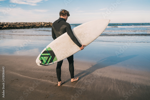 Surfer entering into the water with his surfboard.