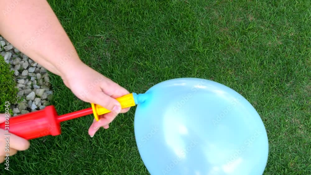 Woman finishing to inflate a blue balloon with a hand pump. Green grass in backgroundd. Close up shot. Woman finishing to inflate a blue balloon with a hand pump. Green grass in backgroundd. Close up shot.