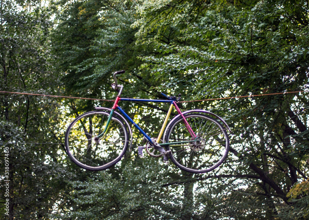 Multi-colored bicycle hanging in the air among the trees in the park