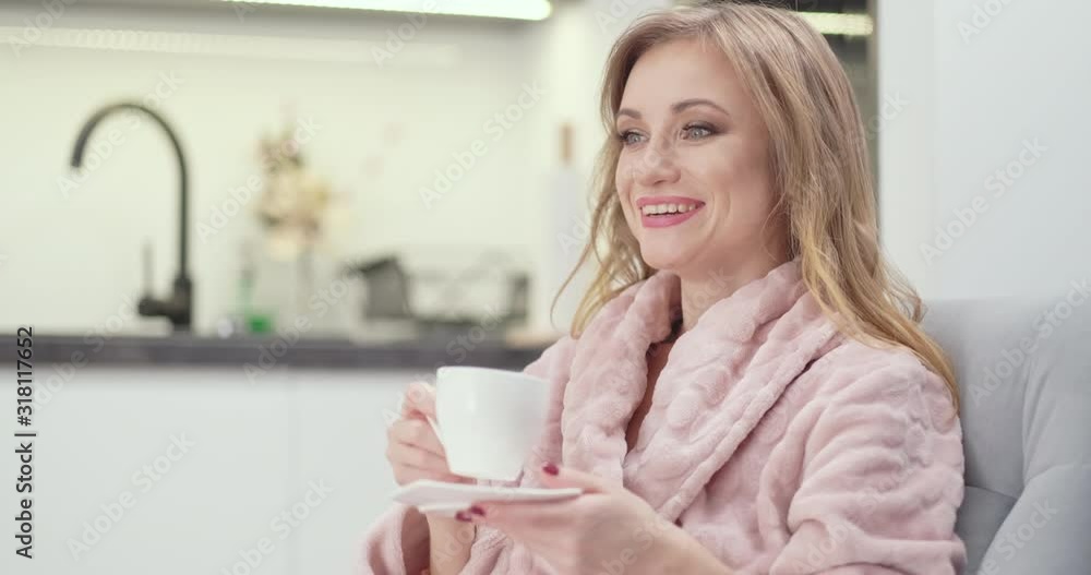 Portrait Beautiful young woman 30s in bathrobe drinking tea, relaxing on sofa, woman is in rest room in the night. She is smiling Portrait Beautiful young woman 30s in bathrobe drinking tea, relaxing on sofa, woman is in rest room in the night. She is smiling