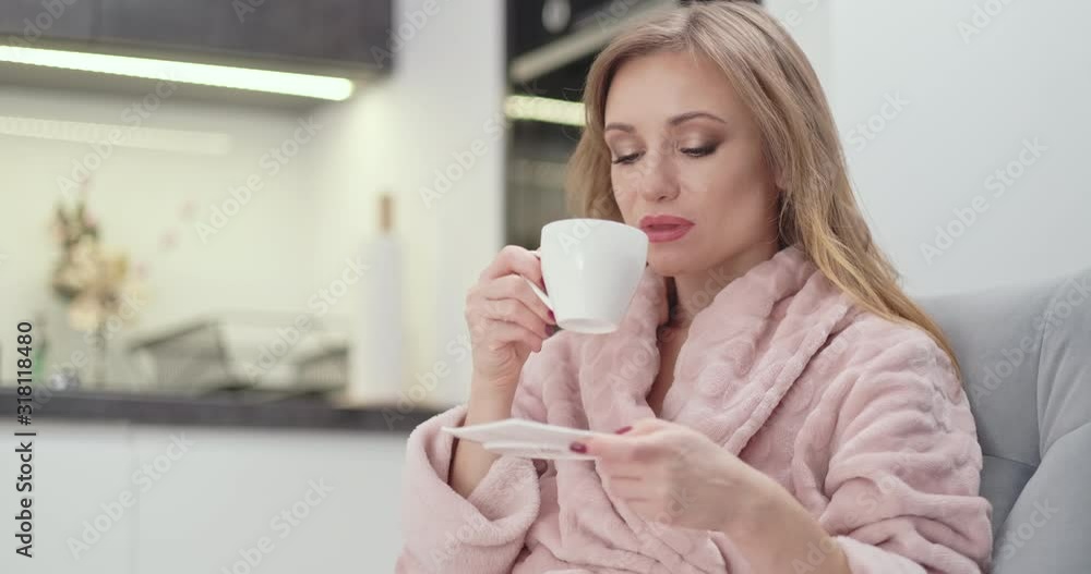 Portrait Beautiful young woman 30s in bathrobe relaxing on sofa, drinking tea, woman is in rest room in the night