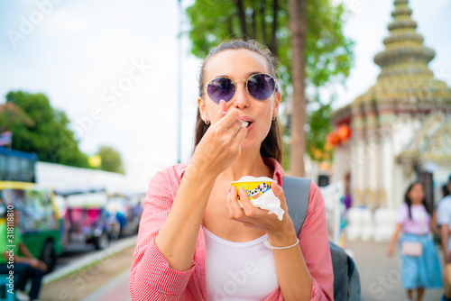 Tourist backpack women eat local coconut milk ice cream while travel in temple
