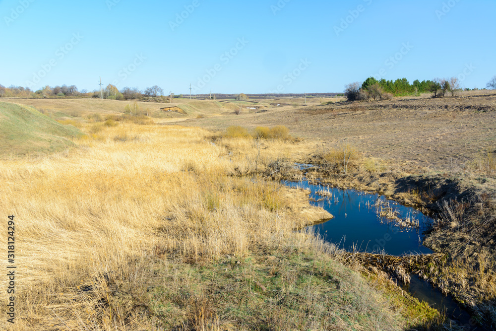 Long-awaited spring creeks flow over ravines and hills on a sunny day. Water rapids and waterfalls of streams among the dry grass. Spring landscape.
