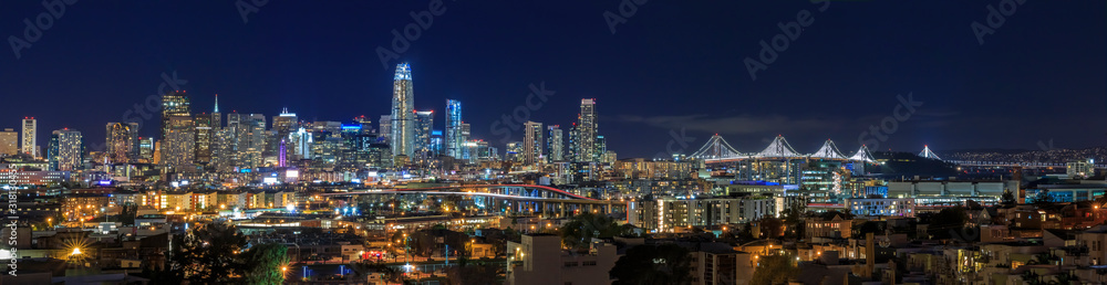 Fototapeta San Francisco skyline night panorama with city lights, the Bay Bridge and trail lights