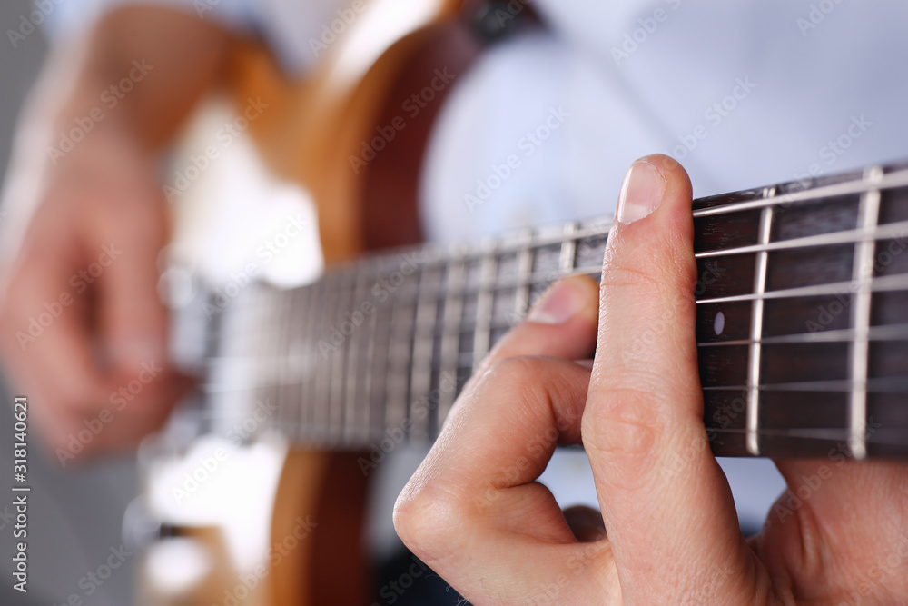 Fototapeta premium Male arms holding and playing classic shape wooden electric guitar closeup. Six stringed learning musical school education art leisure electrical vintage stage shop having fun enjoying hobby concept