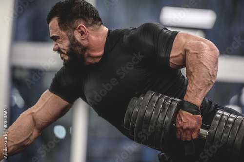 Photos strong young bearded caucasian man in black sportswear lifting heavy weight dumb