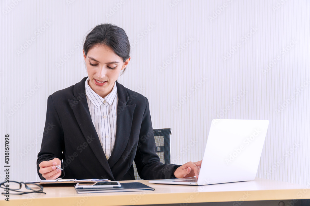 Young businesswoman with document and glasses using laptop and doing some paperwork with pen while working at workstation. Professional woman sitting on table while write something on paper at office. Young businesswoman with document and glasses using laptop and doing some paperwork with pen while working at workstation. Professional woman sitting on table while write something on paper at office.