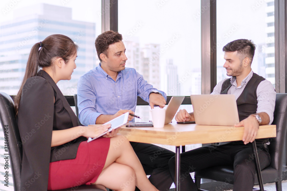 Group business people colleagues talking about planning project in the workplace. Man holding pen with colleagues sitting on desk with laptop while talking work together in office on city background. Group business people colleagues talking about planning project in the workplace. Man holding pen with colleagues sitting on desk with laptop while talking work together in office on city background.