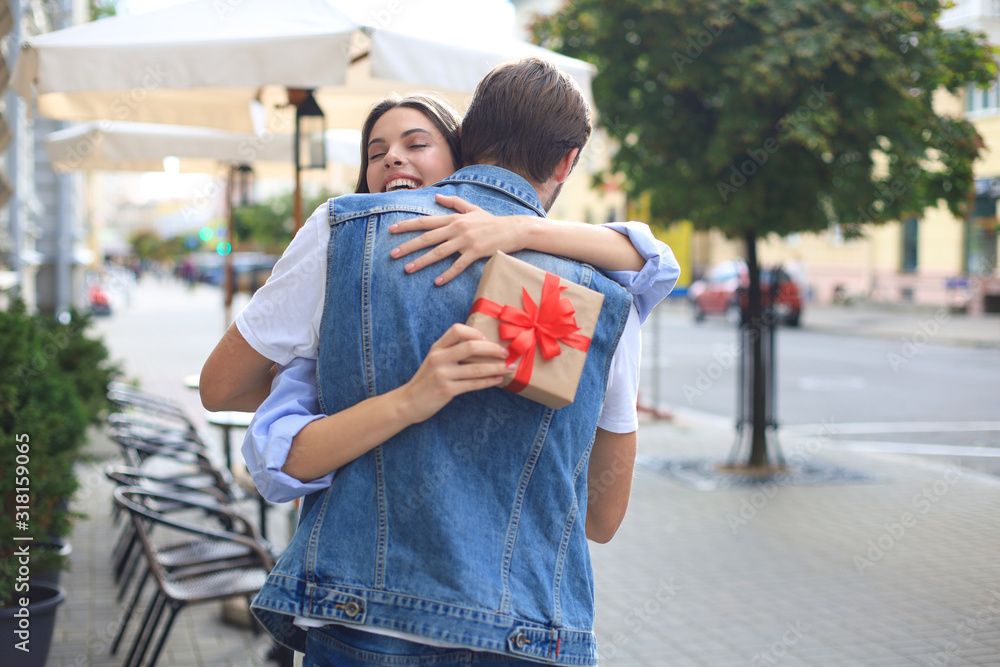 Fototapeta premium Image of attractive woman with present box giving hug to her man.