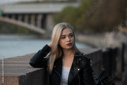 Young fashion blond woman in leather jacket with handbag on city street
