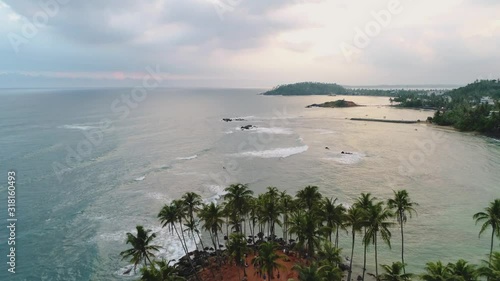 Aerial of Coconut Tree Hill with sunset of background and waves in tropical beach Mirissa, Sri Lanka