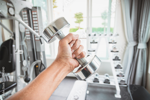Closeup a men's hand holing a dumbbell with his left hand in the gym, Concept for exercise and health care.