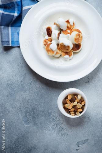 White plate with fried cottage cheese dumplings and sour cream, flatlay on a light-blue stone background with space