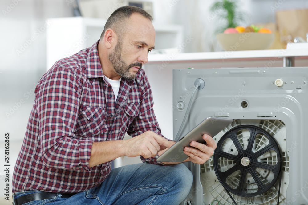 man looking at tablet by broekn down washing machine man looking at tablet by broekn down washing machine