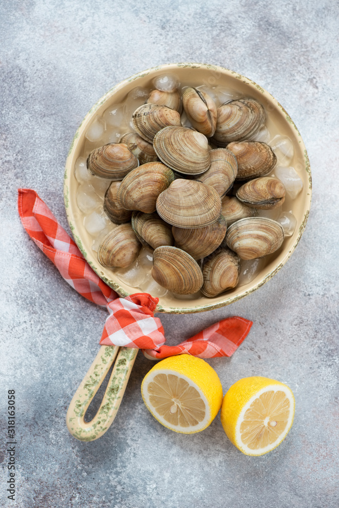 Serving pan with fresh uncooked iced vongole clams and lemon, above view on a beige stone background, vertical shot Serving pan with fresh uncooked iced vongole clams and lemon, above view on a beige stone background, vertical shot
