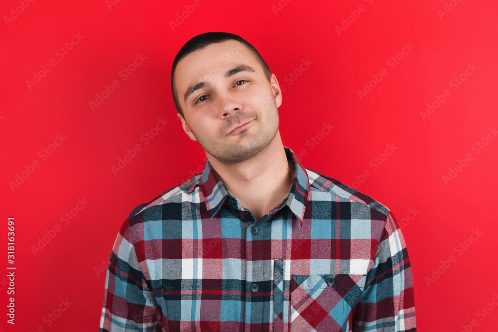 Fototapeta premium The guy in the plaid shirt on the red background. Emotions on the face.