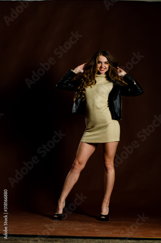 sensual woman in black shiny dress walks to side while looking down and holding her dress, on black background