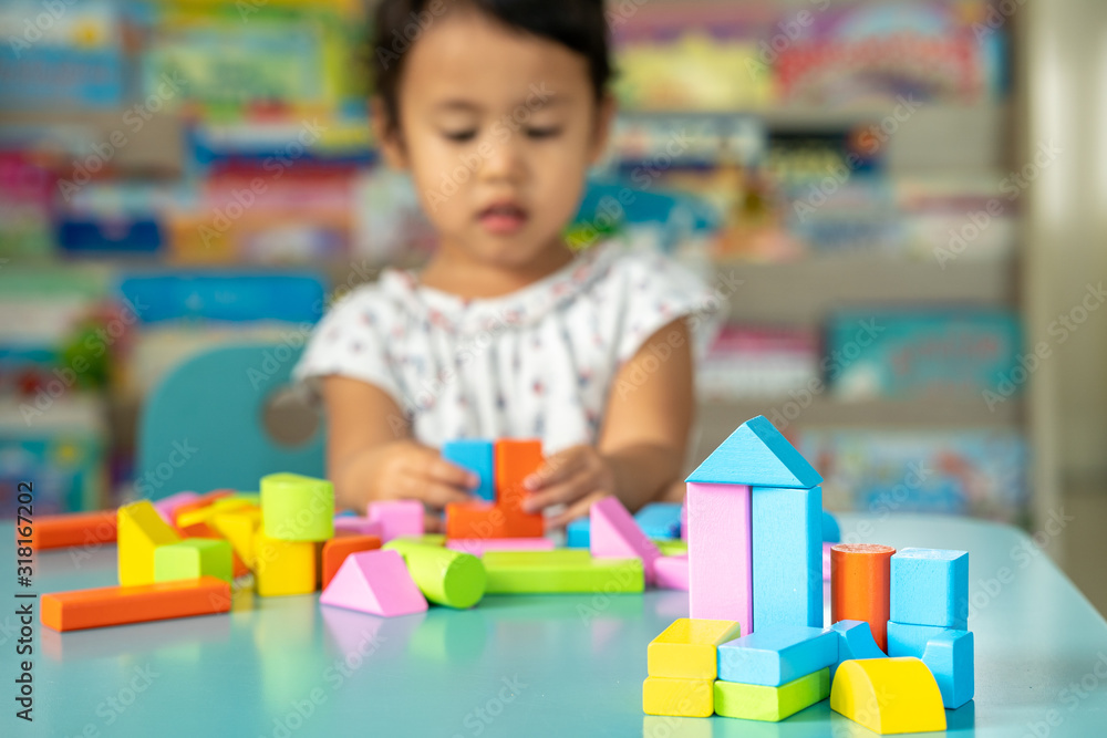 Fototapeta premium Cute little girl playing with multicolor wooden building blocks on blue table.