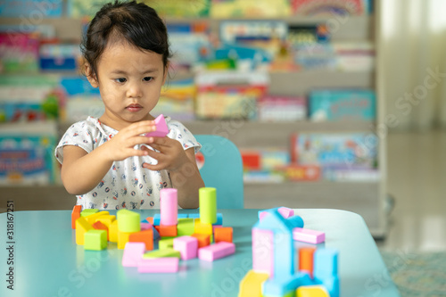 Cute little girl playing with multicolor wooden building blocks on blue table.