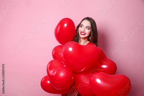 Beautiful elegant young woman with heart shape red air balloons on pink background. © Elena Kratovich