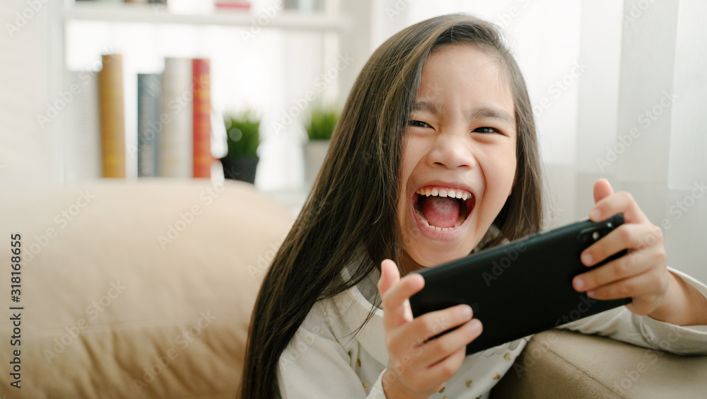 asian little girl playing with smartphone, technology and communication concept - smiling girl texting on smartphone and lying in bed at home asian little girl playing with smartphone, technology and communication concept - smiling girl texting on smartphone and lying in bed at home