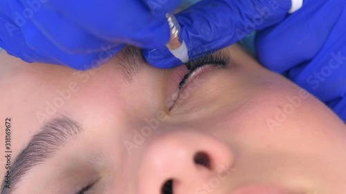 Cosmetologist making permanent eyeliner makeup to woman using tattoo machine, eyes closeup view. Beauty procedure for young girl in beauty clinic salon, hands closeup.