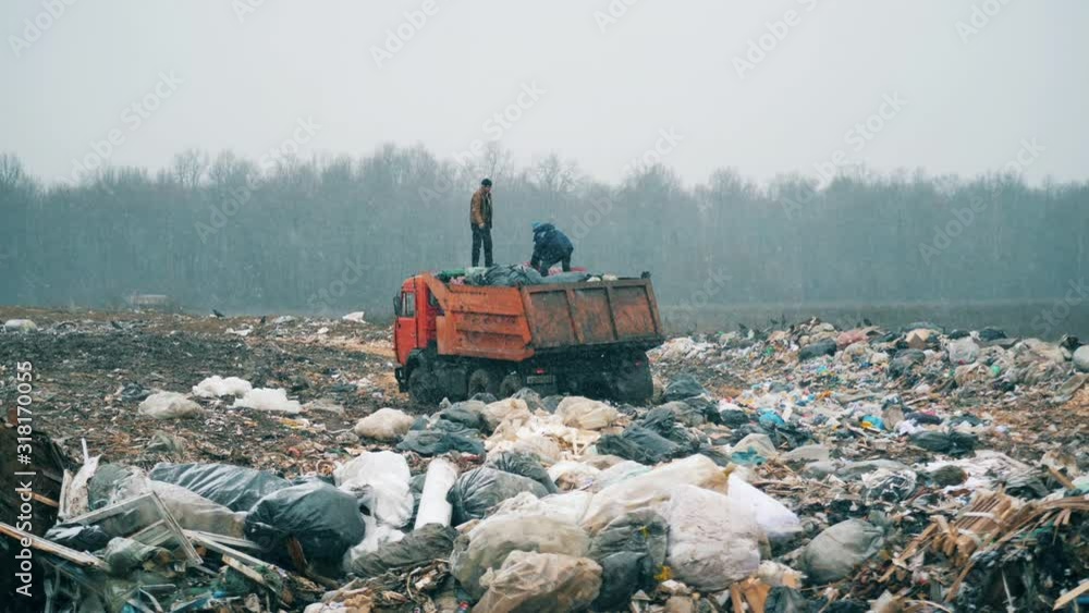 People work at a dump with a truck. People work at a dump with a truck.