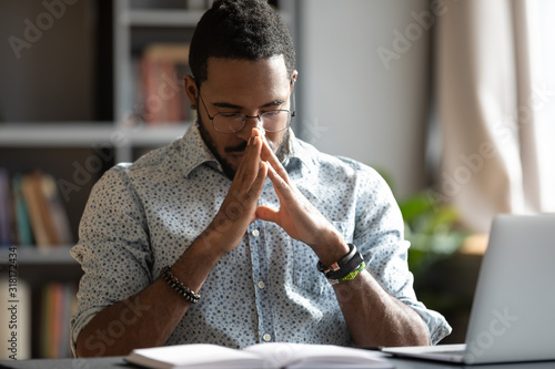 Young african american businessman praying sit at work desk photo