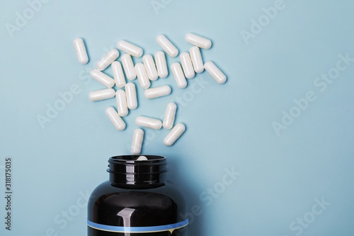 Jar with scattered white medical pills on blue background, photo