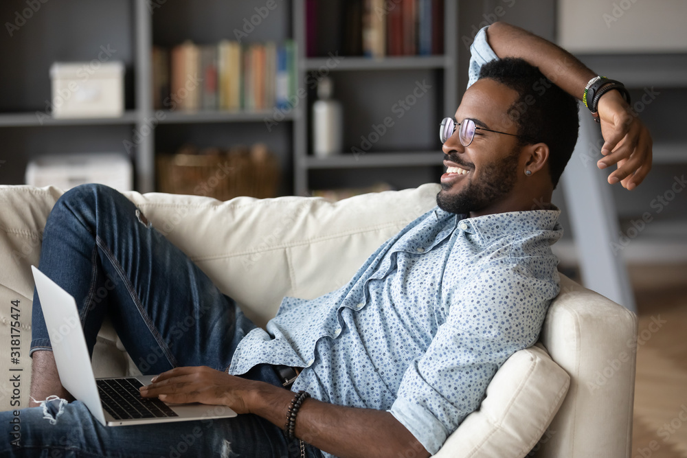 Relaxed african man resting on couch using laptop at home