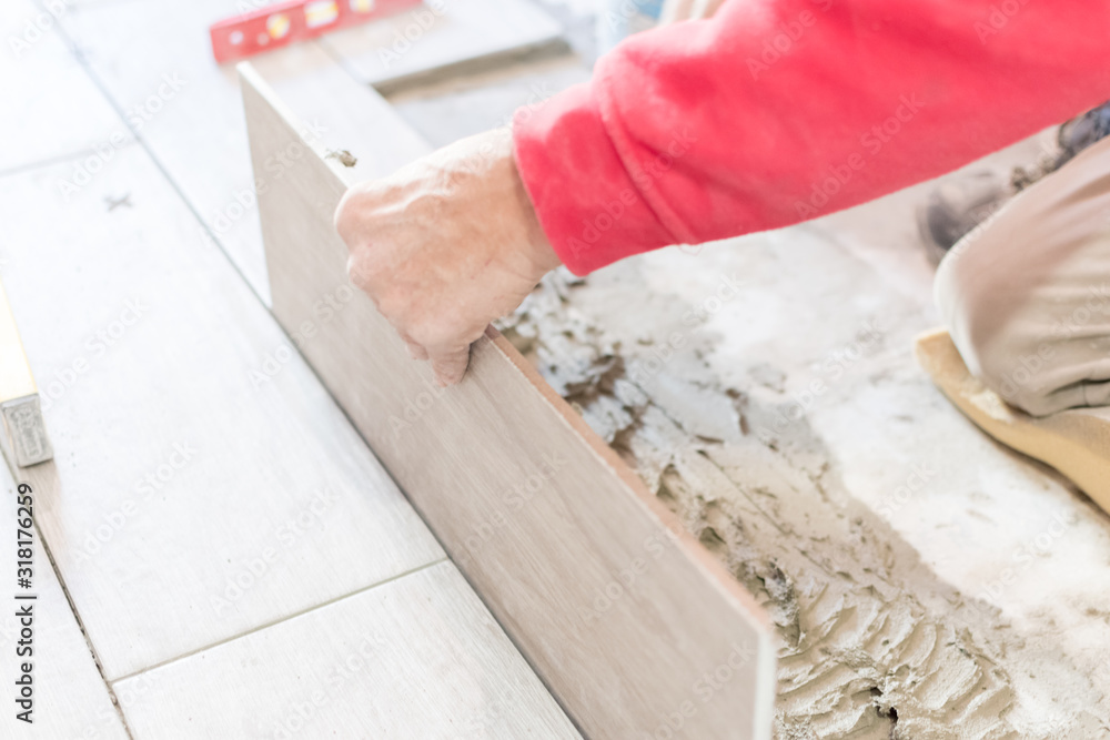 Man installing rectangular shaped floor tiles in kitchen. Applying adhesive before installation and verifying afterwards Man installing rectangular shaped floor tiles in kitchen. Applying adhesive before installation and verifying afterwards