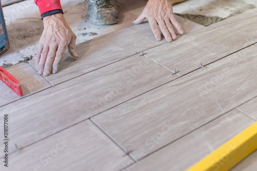 Man installing rectangular shaped floor tiles in kitchen. Applying adhesive before installation and verifying afterwards