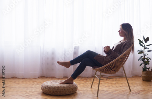 Peaceful woman enjoying hot coffee near window at home