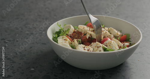 man hand pick salad with mozzarella, cherry tomatoes and frisee leaves in white bowl on terrazzo surface