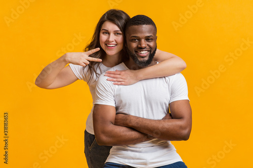 Millennial couple embracing and posing together on yellow background